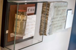 Display of a large glass jar filled with newspapers and a commemoration stone next to it on the wall.