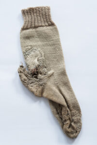 A pale coloured sock showing the signs of being repaired many times.