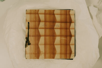 A patterned, square book with the words 'The Hostel' written on it.