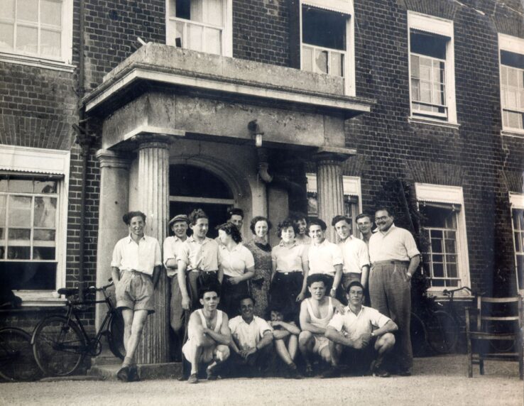 A group of women and men posing in front of a building with a columned entrance.