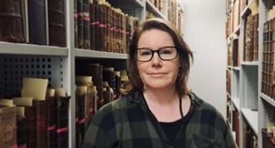 A woman with brown hair between two bookcases holding old books.